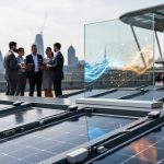 Solar panels with mounted IoT sensors in the foreground and business professionals at a London tech summit background with abstract glowing network connections.